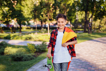 Guy of 9 years old riding skateboard on sunny road in the evening in the city park. Holding fluttering flag of Germany. Happy German day. German language, European education