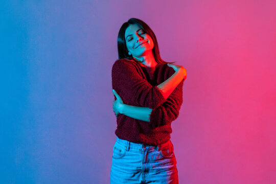 I love myself! Neon light portrait of selfish narcissistic woman embracing herself and smiling with pleasure expression, positive self-esteem and complacency concept. indoor studio shot isolated