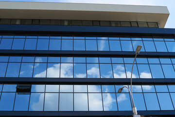 facade of a modern building on a bright Sunny day, blue sky and clouds reflecting in a glass, beautiful exterior of the new building