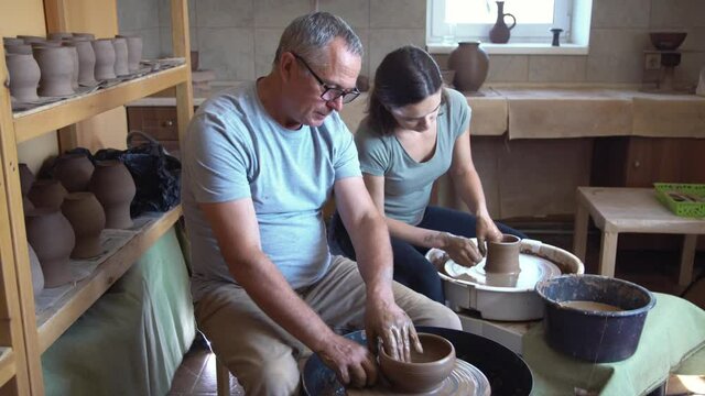 Master and student in pottery workshop. Father teaches daughter at master class. Small family business.