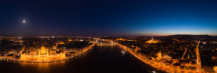 Panoramic aerial drone shot of Danube river with Hungarian Parliament at dusk in Budapest city lights