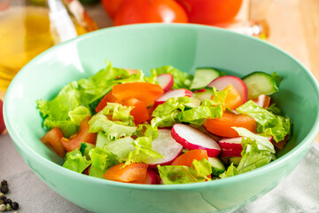 Fresh vegetable salad with olive oil in ceramic bowl on wooden background. Seasonal summer dish of tomatoes, cucumbers and radishes.