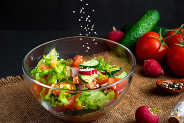 The process of preparing vegetable salad. Seasonal summer dish, vegetarian food on black background.