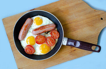 frying pan with fried eggs sausages and tomatoes on the board