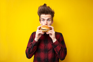 shocked guy eating a burger on a yellow isolated background, surprised hipster eating tasty fast...