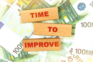 Against the background of euro bills, the text is written on wooden blocks - TIME TO IMPROVE