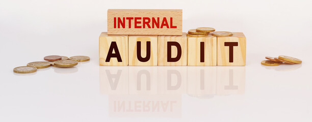On a white reflective surface are coins and wooden cubes with the inscription - INTERNAL AUDIT
