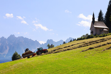 Romantic alpine rural landscape with tractor gathering hay and foggy mountains in background with space for your text