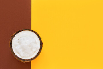 Fresh coconut oil in half of nut on bright yellow-brown backdrop. Top view, copy space.