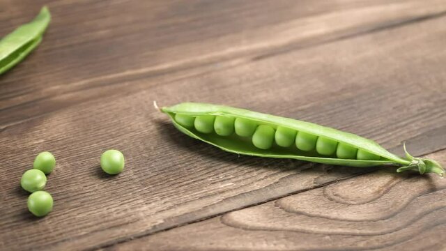 An open pea pod with grains next to other pods on a brown wooden table. Close-up