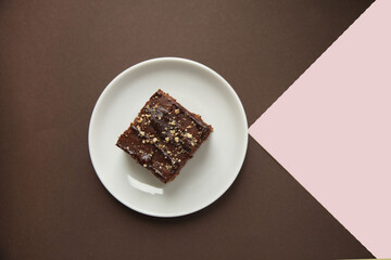 A chocolate piece of cake with nut crumbs on a brown and pink geometric background.