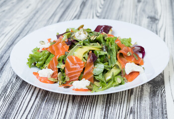 salad with vegetables and red fish on a white plate