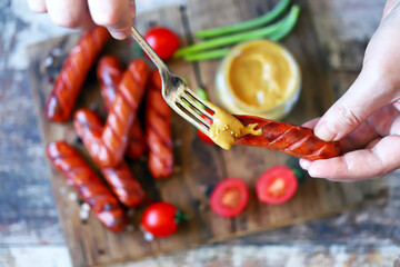 Selective focus. Macro. Sausage and fork with mustard in male hands. Junk food. Fried sausages with mustard.