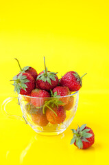 Strawberries in a glass mug on a yellow background, space for text