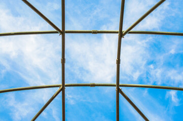 looking up at blue sky through an empty metal plant trellis with a square grid pattern
