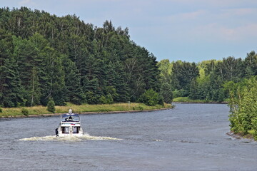 White cabin motor boat slow floating on Moscow navigable canal river water, beautiful rear top view on summer day, Moscow area beautiful river landscape with forest on shores background