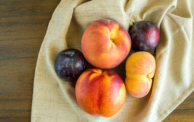 2 donut peaches, 2 plums and a nectarine in a beige linen cloth on a wood background with copy space