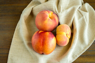 Naklejka na ściany i meble 2 donut peaches and a nectarine in a beige linen cloth on a wood background with copy space