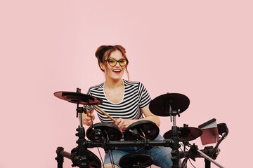 Happy young woman enjoying herself, playing on electric drumset. over pink