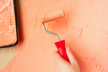 repair roller in the left hand of a person paints wooden plywood in pastel soft orange color, close-up, building content
