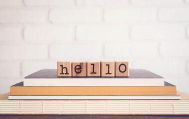 The word HELLO, letters on wooden rubber stamps on top of books with bricks background, blank copy space, vintage minimal style.  Concepts of communication, conversation, language, english greetings.