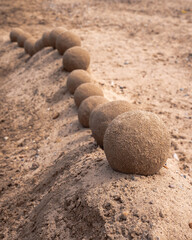 Fototapeta na wymiar Close up view of an undulating sand castle hill or wall with perfectly smooth round balls or spheres of wet sand placed on the ridge that moves up and down in a serpentine shape.