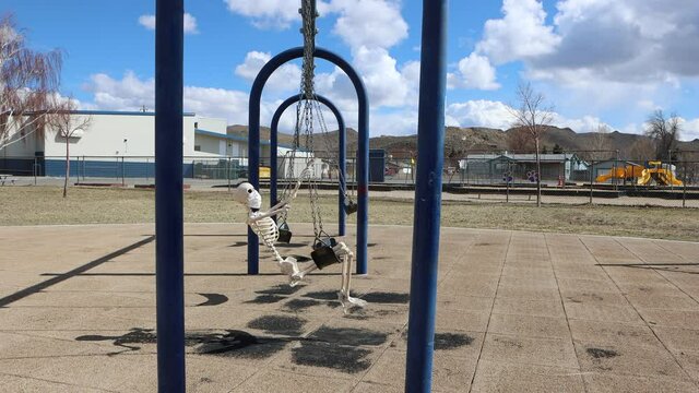 Adult skeleton from side view on park swing wearing a face mask on a beautiful day