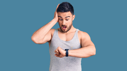 Young handsome man wearing swimwear and sleeveless t-shirt looking at the watch time worried, afraid of getting late