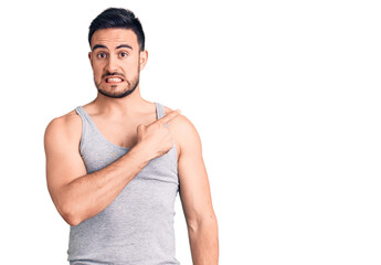 Young handsome man wearing swimwear and sleeveless t-shirt pointing aside worried and nervous with forefinger, concerned and surprised expression