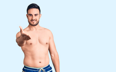 Fototapeta premium Young handsome man wearing swimwear smiling cheerful offering palm hand giving assistance and acceptance.