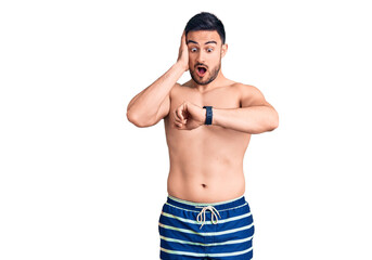 Fototapeta premium Young handsome man wearing swimwear looking at the watch time worried, afraid of getting late