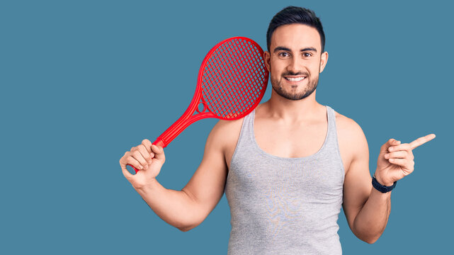 Young handsome man holding tennis racket smiling happy pointing with hand and finger to the side