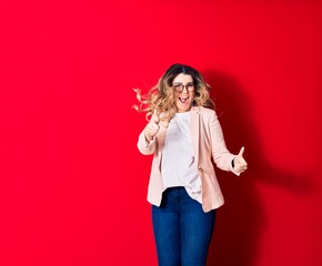 Young beautiful caucasian businesswoman wearing jacket and glasses smiling happy. Jumping with smile on face over isolated red background