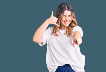 Young caucasian woman wearing casual clothes smiling doing talking on the telephone gesture and pointing to you. call me.