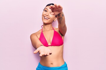 Obraz premium Young woman wearing bikini looking at the camera smiling with open arms for hug. cheerful expression embracing happiness.