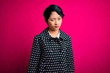 Young beautiful asian girl wearing casual jacket standing over isolated pink background skeptic and...