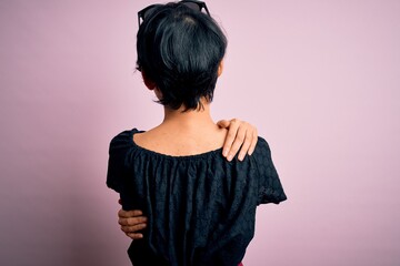 Young beautiful asian girl wearing casual dress standing over isolated pink background Hugging oneself happy and positive from backwards. Self love and self care