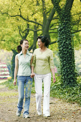 A mother and daughter holding hands walking in the park