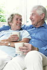 An old couple sitting together on the couch holding cups
