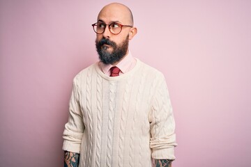 Handsome bald man with beard and tattoo wearing glasses and sweater over pink background smiling looking to the side and staring away thinking.