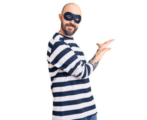 Naklejka premium Young handsome man wearing burglar mask inviting to enter smiling natural with open hand