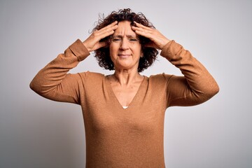 Middle age beautiful curly hair woman wearing casual sweater over isolated white background suffering from headache desperate and stressed because pain and migraine. Hands on head.