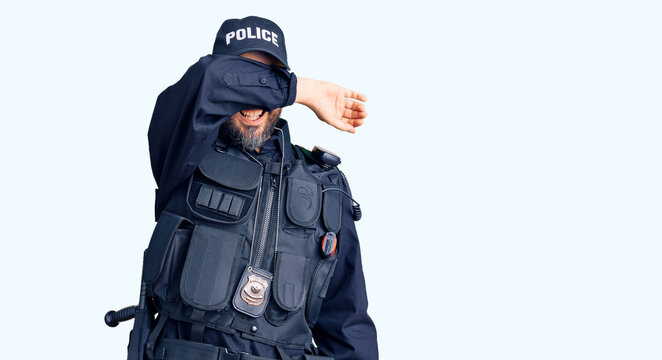 Young handsome man wearing police uniform covering eyes with arm smiling cheerful and funny. blind concept.