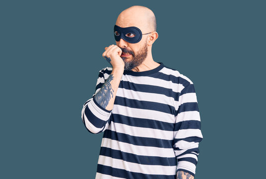 Young handsome man wearing burglar mask looking stressed and nervous with hands on mouth biting nails. anxiety problem.