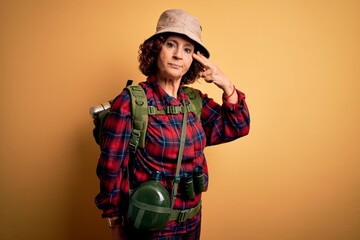 Middle age curly hair hiker woman hiking wearing backpack and water canteen using binoculars Shooting and killing oneself pointing hand and fingers to head like gun, suicide gesture.