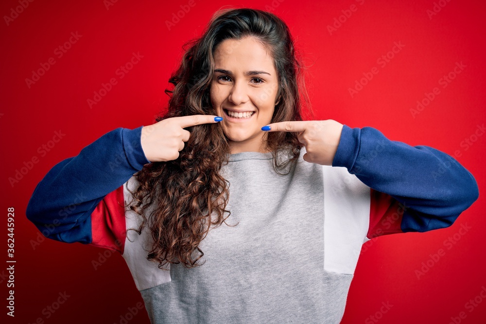 Sticker young beautiful woman with curly hair wearing casual sweatshirt over isolated red background smiling