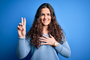 Young beautiful woman with curly hair wearing blue casual sweater over isolated background smiling...