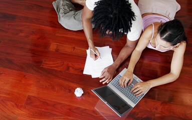Top view of an African American guy and a lady sharing a laptop on the floor