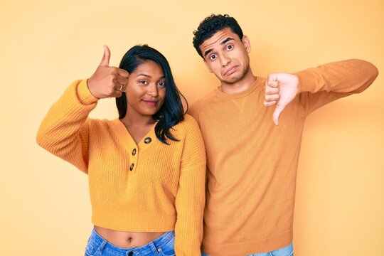 Beautiful latin young couple wearing casual clothes together doing thumbs up and down, disagreement and agreement expression. crazy conflict