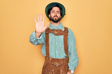 Young handsome man wearing tratidional german octoberfest custome for Germany festival doing stop sing with palm of the hand. Warning expression with negative and serious gesture on the face.